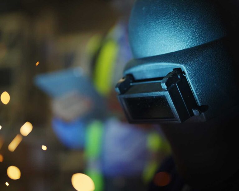 Soldador com máscara de soldagem, mostrando a importância da segurança dos trabalhadores em metalúrgicas.