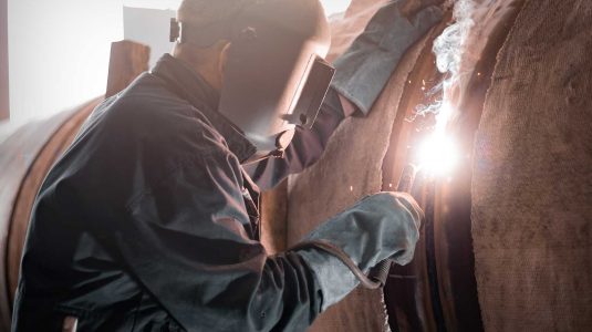 Soldador profissional totalmente equipado com EPI para soldador, como máscara de solda e vestimentas de proteção, enquanto realiza um trabalho de soldagem com segurança.