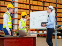 Equipe de segurança do trabalho em reunião com quadro branco planejando a gestão de riscos, aplicando os conceitos do guia de GRO e PGR.