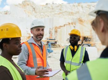 Engenheiro de segurança lidera uma reunião sobre gestão de SST com sua equipe diversa de trabalhadores em uma pedreira.