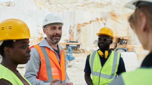 Engenheiro de segurança lidera uma reunião sobre gestão de SST com sua equipe diversa de trabalhadores em uma pedreira.