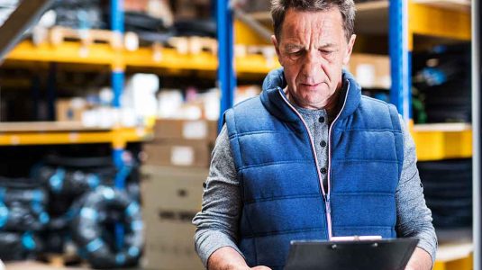 dono de revenda de epi conferindo prancheta no estoque e analisando a necessidade de prospecção de clientes epi para aumentar o giro de produtos