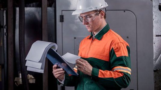 profissional-de-sst-com-capacete-e-uniforme-analisando-documentos-sobre-higiene-ocupacional-em-uma-prancheta-dentro-da-industria