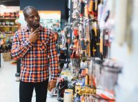 homem-negro-com-camisa-xadrez-escolhendo-produtos-no-corredor-de-uma-loja-de-ferragens-e-ferramentas