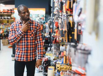homem-negro-com-camisa-xadrez-escolhendo-produtos-no-corredor-de-uma-loja-de-ferragens-e-ferramentas