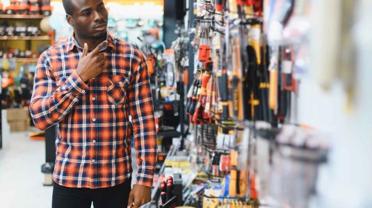 homem-negro-com-camisa-xadrez-escolhendo-produtos-no-corredor-de-uma-loja-de-ferragens-e-ferramentas