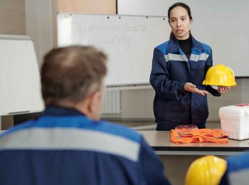 profissional com uniforme azul segurando um capacete amarelo enquanto orienta a equipe ilustrando a comunicação clara e o marketing pessoal para profissionais de sst na prática.