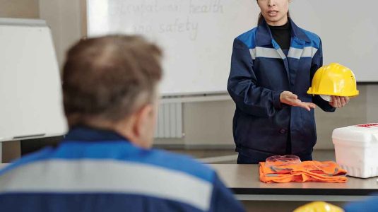 profissional com uniforme azul segurando um capacete amarelo enquanto orienta a equipe ilustrando a comunicação clara e o marketing pessoal para profissionais de sst na prática.