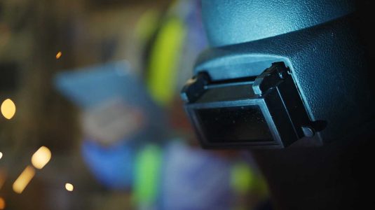 Soldador com máscara de soldagem, mostrando a importância da segurança dos trabalhadores em metalúrgicas.