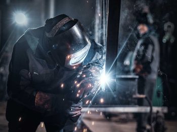 soldagem-e-aposentadoria-especial Soldador profissional usando máscara de proteção e luvas de raspa durante trabalho com solda industrial