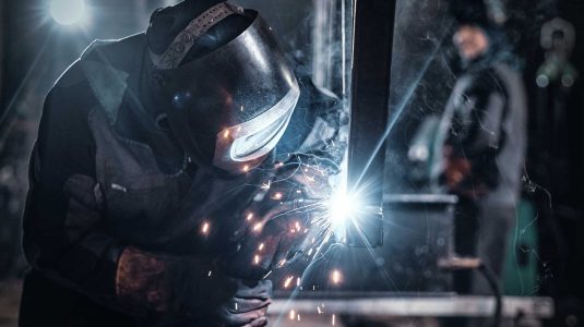 Soldador profissional usando máscara de proteção e luvas de raspa durante trabalho com solda industrial