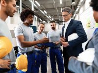 gerente em traje social conversa com operários em ambiente industrial para ilustrar como unir gerência e colaboradores na segurança do trabalho com foco em prevenção e uso de epis